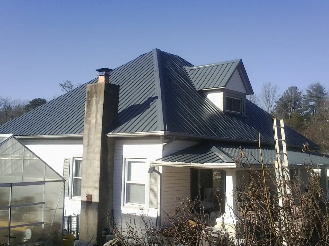 Dark blue standing seam metal roof on a white farmhouse with dormer — Slate & Tile Roof Repair by Roofing Brothers in Uehling