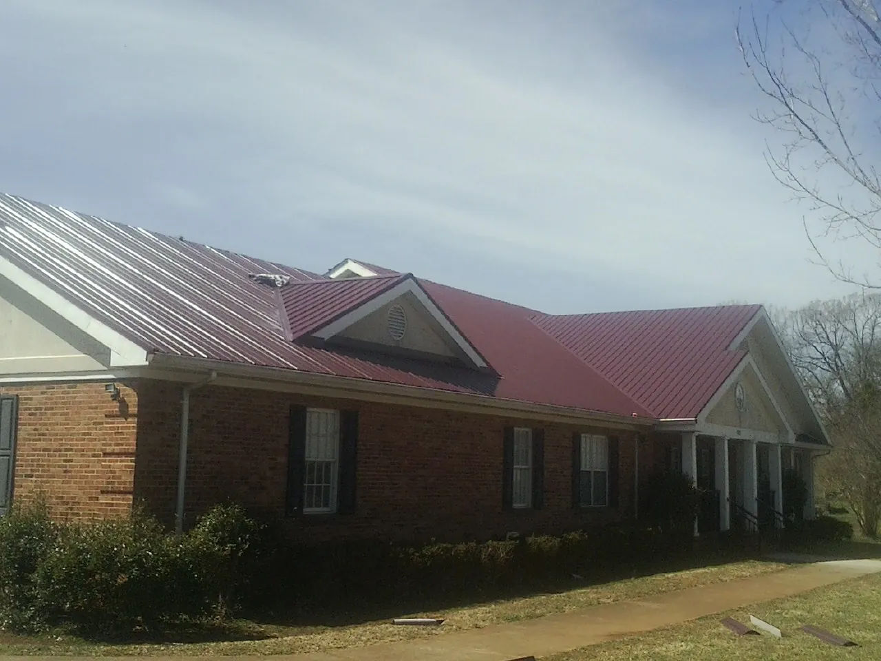Red metal roof with gabled entries on a long brick building, from a Hail Damage Roof Repair job in Uehling