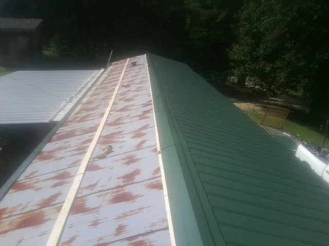 Old rusted panels beside newly installed green metal roofing — Wind Damage Roof Repair by Roofing Brothers in Uehling
