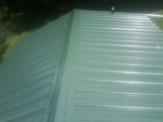 New green metal panels meeting at the ridge of a roof — Flat Roof Repair work by our crew in Uehling