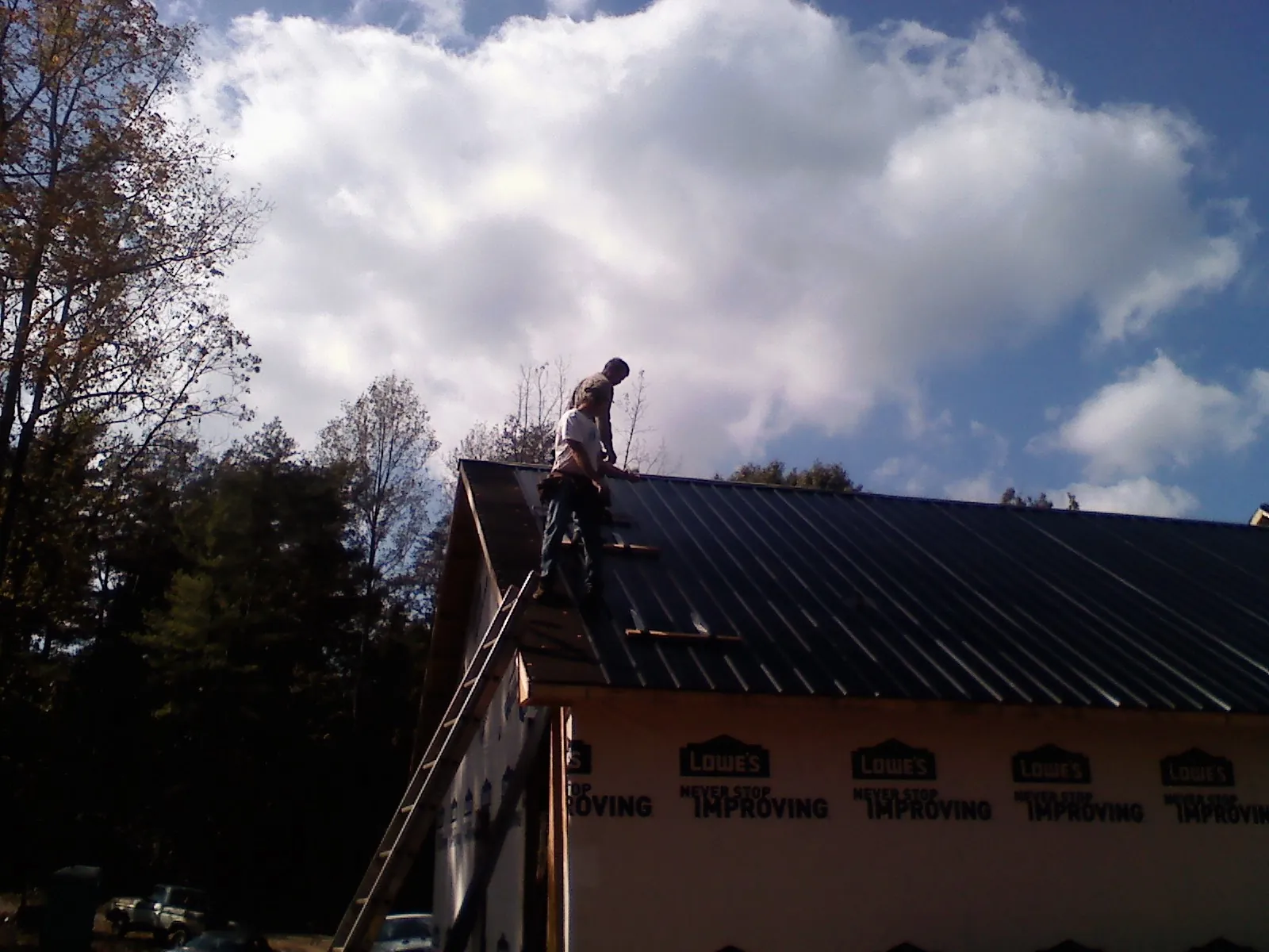 Roofer fastening dark metal panels high against a cloudy sky, from a Roof Inspection job in Uehling