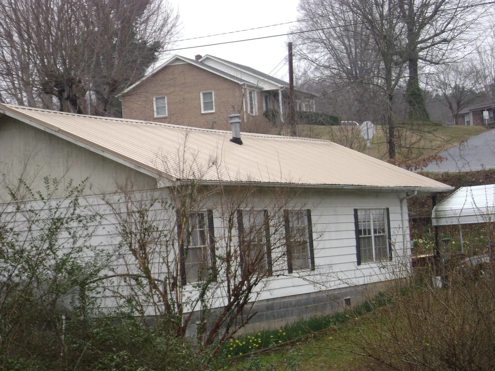 Tan metal roof on a white sided house set into a hillside — Commercial Roofing by Roofing Brothers in Uehling