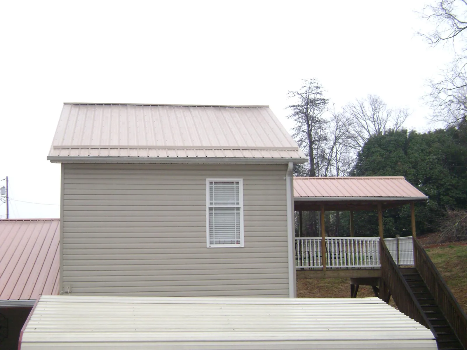 Tan metal roofs on a two story addition and attached porch, from a Roof Replacement job in Uehling
