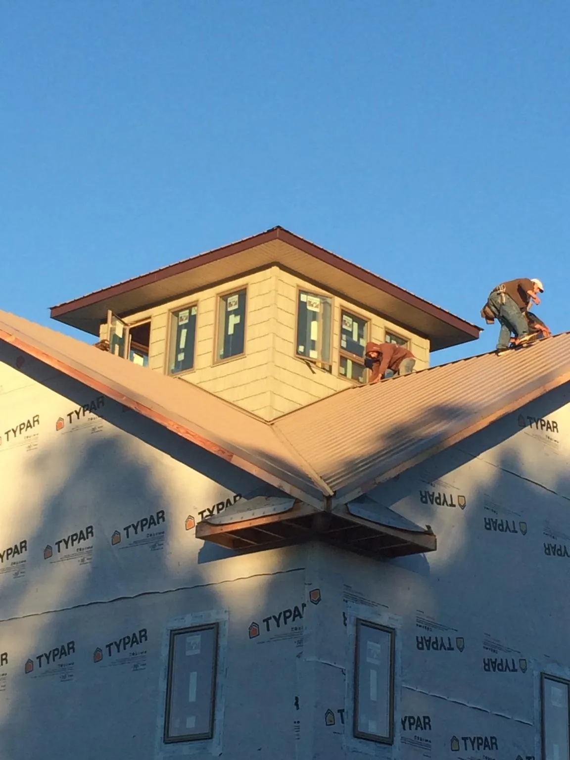 Roofers working around a rooftop cupola on a new metal roof at sunset — Roof Waterproofing in Uehling by Roofing Brothers
